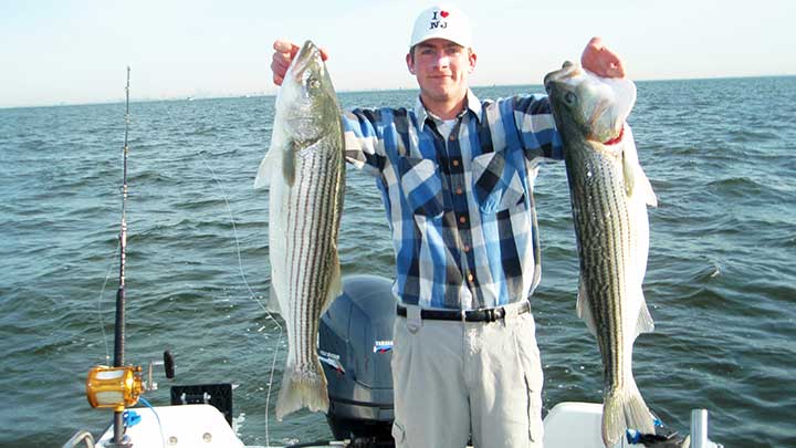 captain cody holding two big striped bass in new jersey